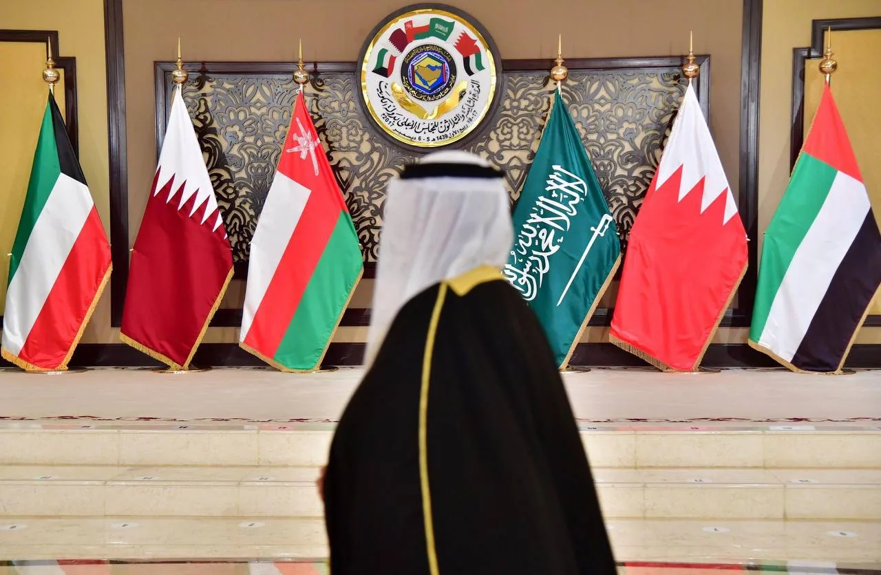 Gulf national in traditional dress standing before GCC country flags in a formal setting